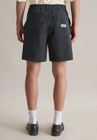 Zwarte katoenen shorts met een elastische tailleband, zijzakken en een achterzak met een label. Afgewerkt met een nette zoom.