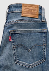 Πίσω όψη μπλε τζιν παντελονιών που δείχνει μια ραμμένη πίσω τσέπη με μια κόκκινη ετικέτα Levi's και μια καφέ δερμάτινη ετικέτα Levi Strauss & Co.