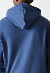 Sweat-shirt à capuche bleu avec une texture douce, présentant une couture centrale et une coupe décontractée. La capuche est fixée à l'arrière.