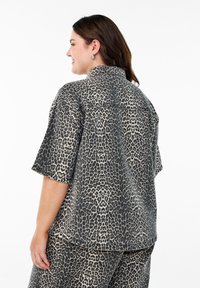 Chemise imprimée léopard en tissu doux, avec des manches courtes, un col, et une coupe décontractée avec un ourlet légèrement arrondi.