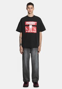 Czarna, oversize T-shirt z czerwoną grafiką oraz napisem "PROSTO WILD WORLD". Połączona z wyblakłymi szarymi dżinsami i wzorzystymi butami w kolorze czerwono-czarnym.