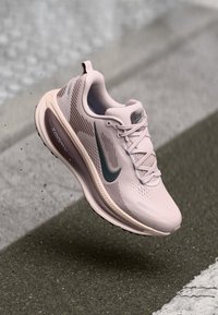 Jasnoróżowy but sportowy z teksturowanym wierzchem, ciemnozielonym logo Swoosh, sznurowadłami oraz wyściełaną podeszwą z brandingiem "ZoomX".