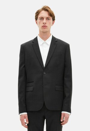 Ciemnoszary garnitur z subtelnym wzorem w kratę, zapinany na jeden guzik, z klapami w kształcie notcha i dwoma przednimi kieszeniami. Nosił go z białą koszulą z kołnierzykiem.