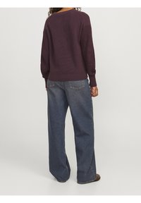 Maglione a maglia di un viola scuro, con un design strutturato e polsini a coste, abbinato a jeans blu a taglio classico, dalla vestibilità ampia.