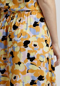 Rochie florală cu flori mari portocalii, galbene și negre pe un fundal deschis. Talie elastică cu un croi fluid și textură moale.