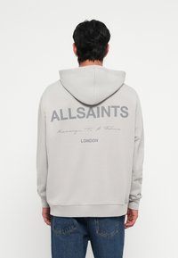 Sweatshirt à capuche gris avec le texte au dos "ALLSAINTS" et "Message à un père" au-dessus de "LONDRES" ; présente des poignets côtelés et une coupe décontractée.