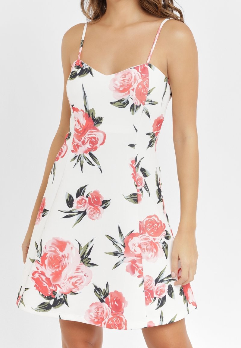 Blommig klänning med vit bakgrund, prydd med stora rosa rosor och gröna blad. Tunna axelband och utställd A-linjeform.