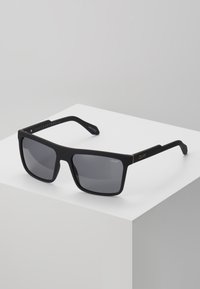 Ochelari de soare rectangulari negri cu lentile închise, textură mată și accente aurii pe brațe. Prezintă branding gravat pe laturi.
