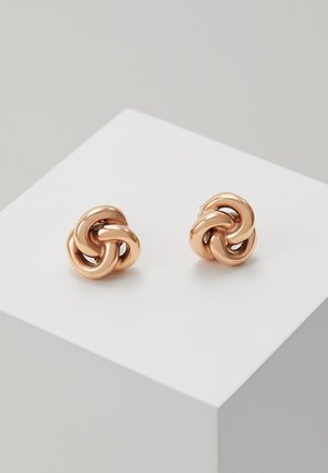 Paire de boucles d'oreilles clous en forme de nœud en or rose brillant, présentées sur un cube blanc sur un fond gris clair.