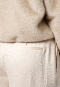 Beige gebreide trui met een zachte textuur, gedrapeerd over lichtbeige textuurbroek met een achterzak en subtiele naaddetails.