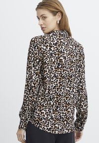 Blusa a maniche lunghe in tessuto leggero con motivo a stampa leopardo in nero, marrone e beige. Presenta un orlo curvo e polsini con bottoni.