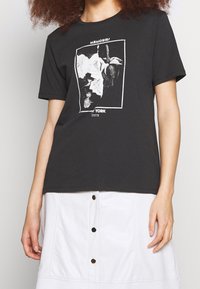 Black cotton t-shirt featuring a white graphic print with flowers and "MEMORIES" text, worn with a white skirt with button details.