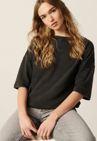 Zwarte oversized t-shirt met korte mouwen, gemaakt van katoen, met een comfortabele pasvorm en subtiele vervaging. Gecombineerd met lichtgrijze jeans.