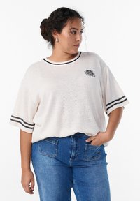 Camisa de punto oversize color beige claro con acentos de rayas negras en las mangas y el escote, con un pequeño diseño gráfico en el pecho.