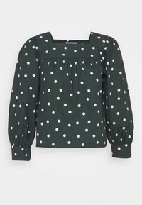 Blouse verte à pois blancs avec un décolleté carré, des manches longues bouffantes et une taille froncée. Présente des pois blancs uniformément répartis.