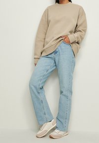 Felpa oversize beige, jeans dritti blu chiaro e sneakers beige con accenti chiari. L'outfit presenta una vestibilità rilassata e una texture morbida.