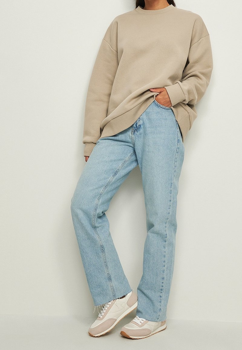 Felpa oversize beige, jeans dritti blu chiaro e sneakers beige con accenti chiari. L'outfit presenta una vestibilità rilassata e una texture morbida.