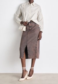 Brun denim midi-nederdel med slids foran, parret med en stribet beige skjorte og lyse spidse hæle. Lille crossbody-taske.