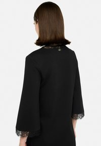 Zwart jurk met kantafwerking op de mouwen en de halslijn; heeft een zachte textuur en een subtiel logo op de achterkant.