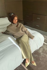 Béžová zipsová bunda, krémové široké nohavice a svetložlté špičaté lodičky. Mäkké prehozy a textúrovaný koberec vytvárajú neutrálny pozadie.