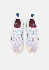 Zapatillas deportivas blancas con parte superior de malla, detalles en azul y amarillo, suela verde y forro rojo y granate. Presentan cordones y detalles de marca.