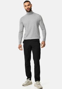 Grauer Rollkragenpullover, enganliegend, kombiniert mit schwarzen Hosen. Tan- und graue Sneaker vervollständigen das Outfit. Glatte Textur, minimale Designelemente.