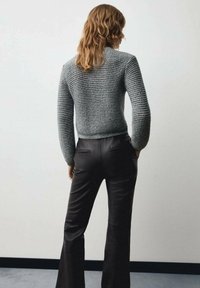 Pulover gri din tricot cu cusături texturate, asortat cu pantaloni negri evazați. Puloverul are un design ajustat și mâneci lungi.