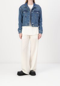Kurtka dżinsowa w jasnoniebieskim kolorze, z zapięciami na guziki, dwoma kieszeniami na piersi i klasycznym kołnierzem, zestawiona z kremowymi, szerokimi spodniami.