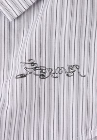 Striped cotton fabric in gray and white with delicate black embroidered text "Former." Features a traditional collar design.