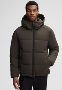 Giacca a vento verde scuro con cappuccio, dotata di zip frontale e design trapuntato. Tessuto liscio, polsini elasticizzati e tasche laterali.