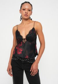 Camisole in pizzo nero con scollatura a V profonda, stampa floreale trasparente e spalline regolabili. Abbinato a jeans neri con dettagli borchiati.