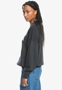 Tumehall oversized sweatshirt ribide tekstuuriga, langenud õlgade ja ümarate kaelustega, koos kõrge talje siniste teksadega.