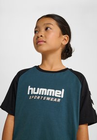 Kortärmad t-shirt i teal och svart med rund halsringning. Har "hummel SPORTSWEAR"-logotyp i vitt på framsidan. Klassisk raglan-design.
