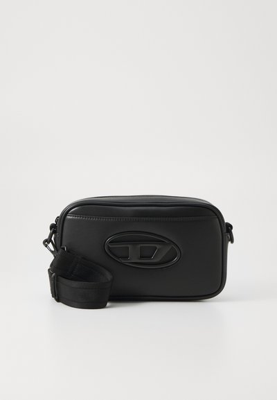 Sac à épaule en cuir noir avec une forme rectangulaire, une surface texturée, un logo embossé et une bandoulière ajustable. Fermeture éclair en haut.