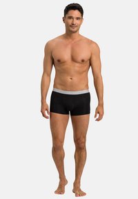 Černé boxerky s šedým páskem s názvem značky "HANRO", vyrobené z hladkého, elastického materiálu. Model stojí naboso.