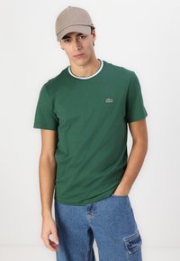Tricou din bumbac verde, cu guler rotund și margine albă în contrast, având un mic logo brodat pe partea stângă a pieptului. Croi lejer.