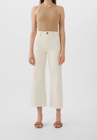 Vaalean beige ribattu toppi yhdistettynä kermaisiin leveälahkeisiin farkkuihin, joissa on raaka helma ja yksi etunappi. Ruskeat sandaalit.