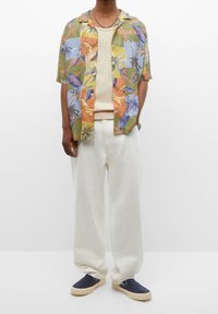 Chemise tropicale à manches courtes avec motifs multicolores de feuilles et d'oiseaux, associée à un pantalon large crème et des chaussures navy à enfiler.
