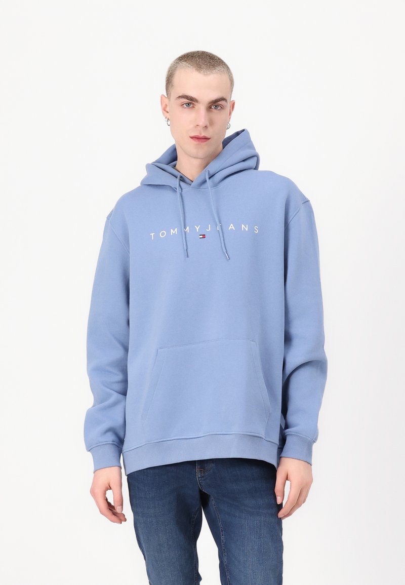Lichtblauwe hoodie met een voorzak in kangoeroestijl, capuchon met trekkoord en een witte logo met de tekst "TOMMY JEANS" over de borst. Zacht materiaal.