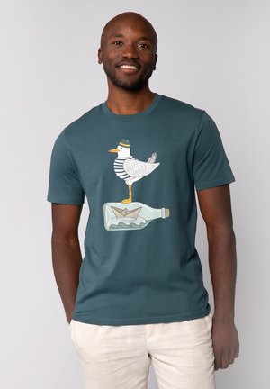 Heren T-shirt met korte mouwen in teal katoen, met een grafische afbeelding van een witte vogel in een gestreepte shirt die op een fles staat met een papieren bootje erin.