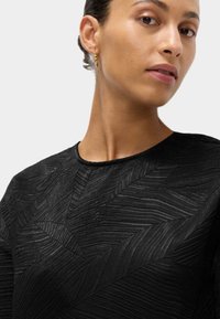 Top nero con texture caratterizzato da un motivo geometrico con linee orizzontali in rilievo. Collo rotondo con lieve lucentezza e senza hardware visibile.