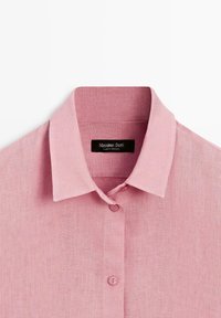 Rosa Leinen-Hemd mit Knöpfen und spitzem Kragen, die oberen drei Knöpfe sichtbar, mit einem schwarzen Etikett, auf dem "Massimo Dutti" steht.