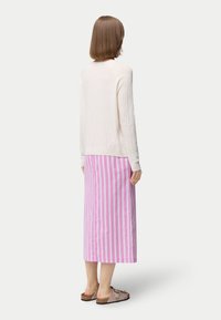 Vit texturerad långärmad topp ihop med en rosa och vit randig midjekort kjol; modellen bär beige sandaler, sedd bakifrån.