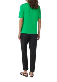 Green short-sleeve T-shirt, black tapered pants, and black flat shoes. Simple design with a relaxed fit and smooth texture.