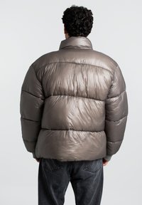 Metalinis taupe spalvos pūkuotas švarkas su aukštu apykakle, siuvinėtu dizainu ir elastinėmis rankovėmis. Ypatybė - lygus, blizgus paviršius ir laisvas siluetas.