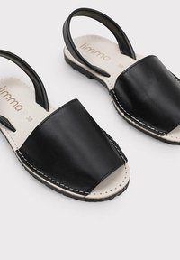 Sandalias de cuero negras con diseño de puntera cerrada y parte trasera abierta, con costuras blancas y una suela texturizada para un mejor agarre.