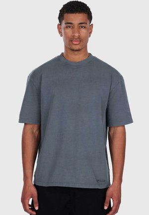 T-shirt grigio oversize in cotone, con scollatura a girocollo e maniche corte. Un piccolo logo vicino all'orlo aggiunge un tocco di dettagli.