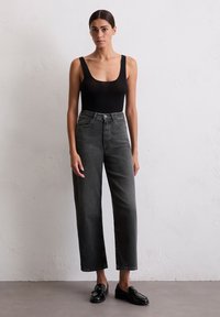 Czarny body na szerokich ramiączkach, spodnie z wysokim stanem w luźnym kroju w ciemnoszarym kolorze oraz błyszczące czarne mokasyny. Prosty design, brak widocznych wzorów.