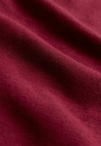 Burgundská bavlnená tkanina s jemnou ribovanou textúrou, ktorá vykazuje mäkký spád a jemný lesk. Povrch má hladký, rovnomerný finiš.