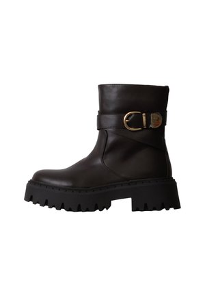 Bottine noire en cuir avec semelle épaisse à crampons et bride à boucle dorée autour de la tige supérieure, vue latérale sur fond blanc.